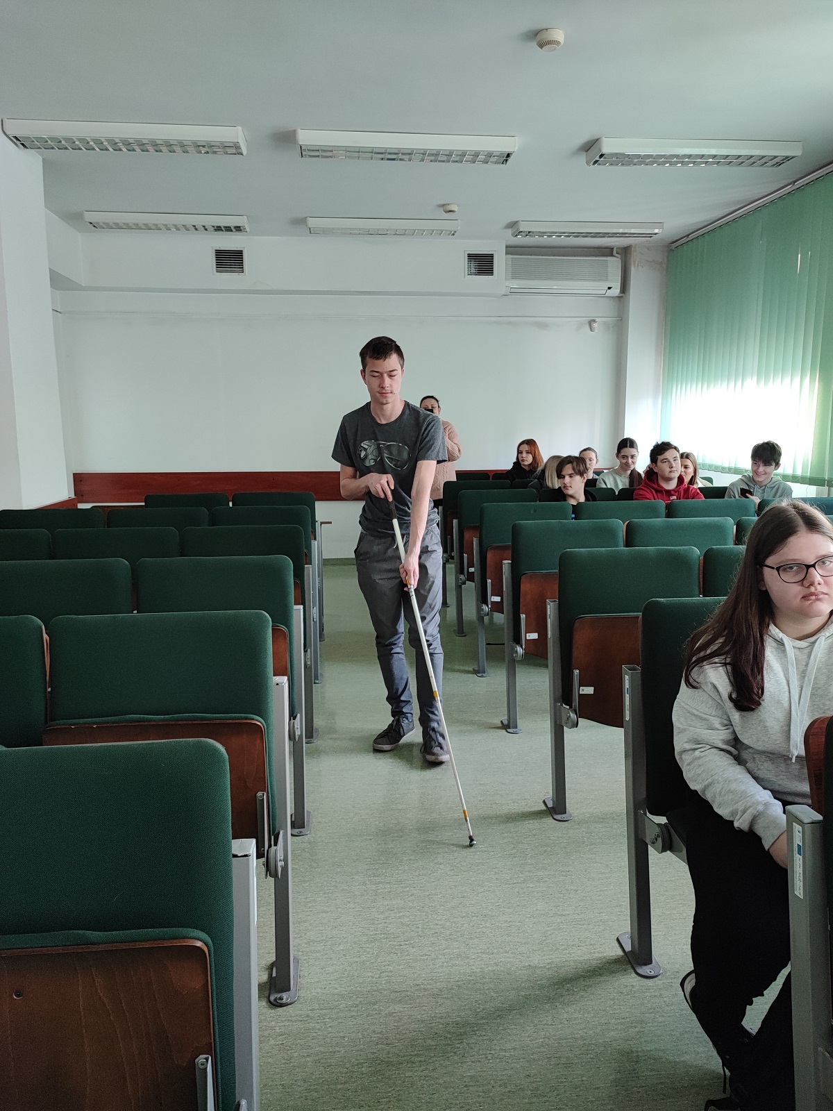 Uczeń próbuje przejść po sali wykorzystując laskę dla osób niewidomych.