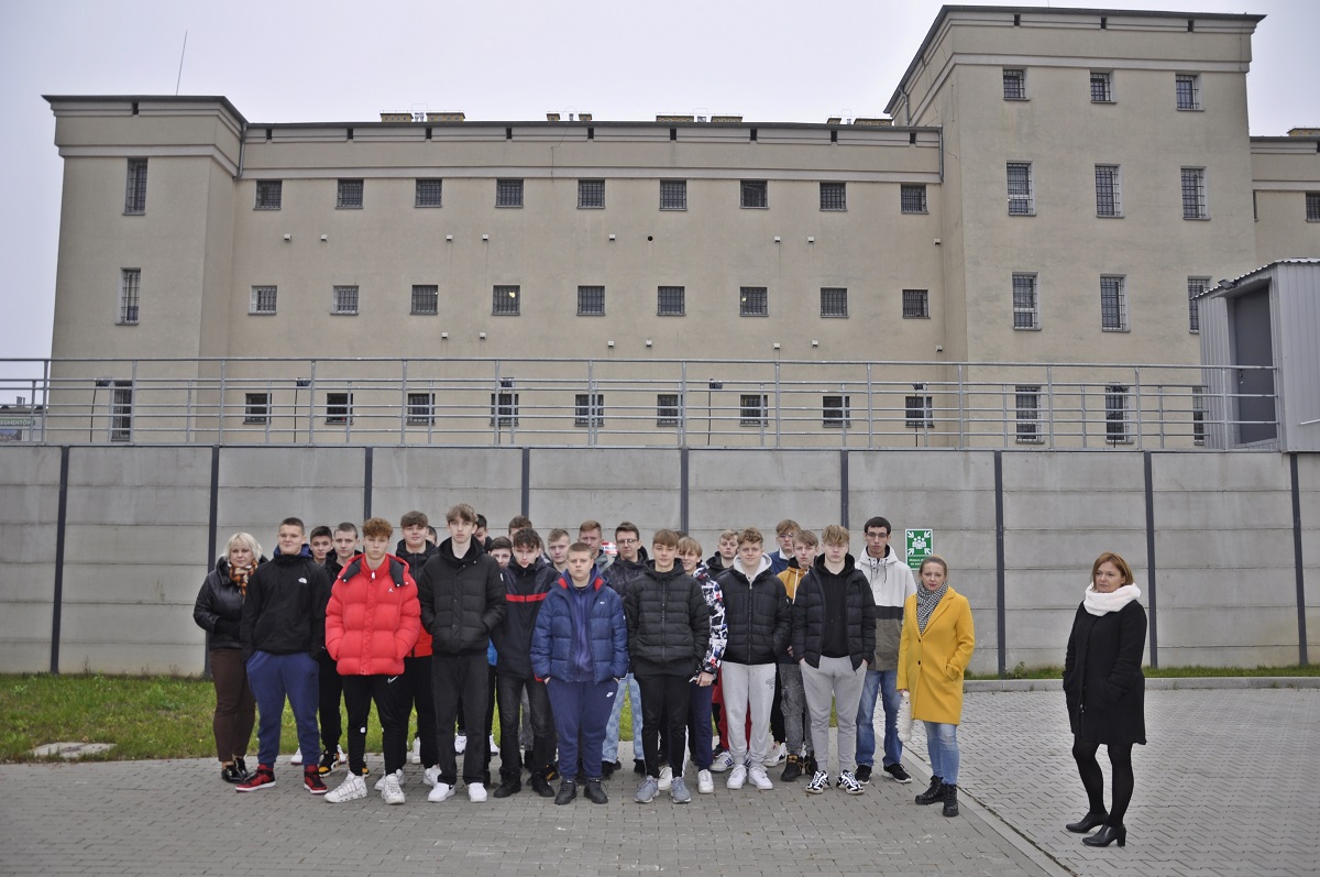 Grupa uczniów wraz z nauczycielami. W tle budynek więzienia.